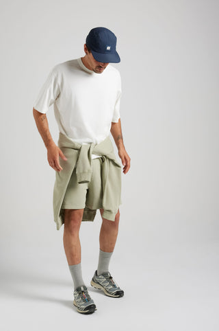 Persona che indossa Essential Sunwashed Sweatshorts in Seagrass, abbinati a una t-shirt bianca e una cap. | TP_IMAGE_TYPE=MODEL_FRONT