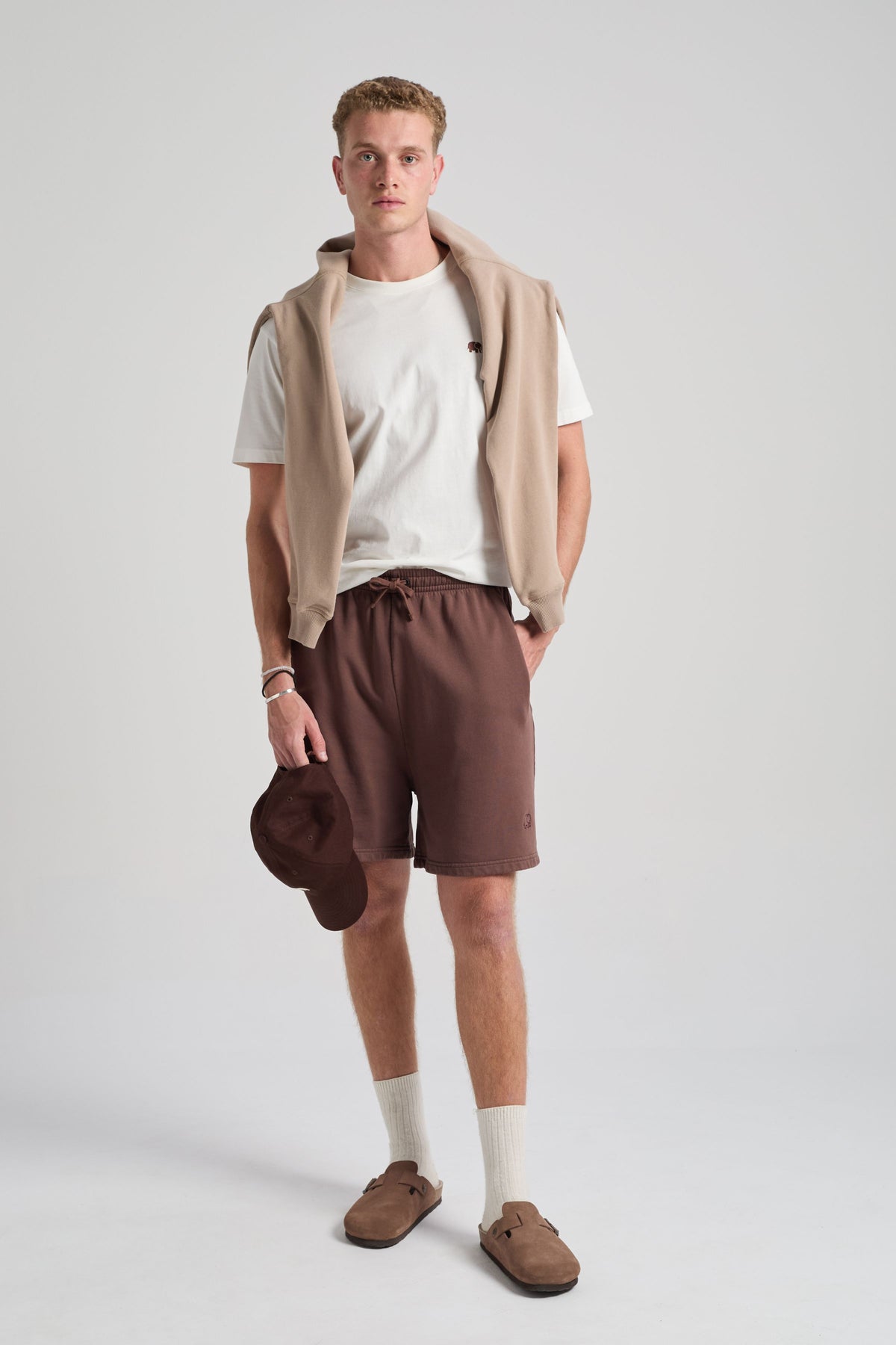 Persona che indossa Essentials Sweatshorts in Shaved Chocolate, abbinati a un gilet beige e a un berretto marrone | TP_IMAGE_TYPE=MODEL_FRONT
