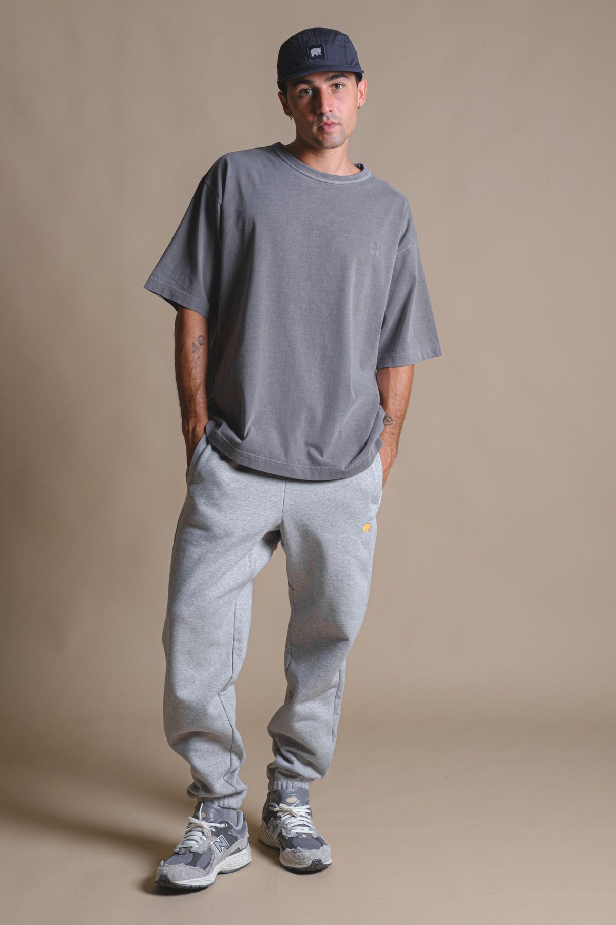Personne portant le pantalon de jogging Organic Essential Sweatpants Heather Grey avec une coupe décontractée, associé à un t-shirt gris décontracté et des baskets | TP_IMAGE_TYPE=MODEL_FRONT