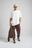 Persona che indossa gli Essential Sweatpants in Shaved Chocolate, abbinati a una t-shirt bianca e a un cappellino beige, in piedi davanti a uno sfondo neutro. | TP_IMAGE_TYPE=MODEL_FRONT
