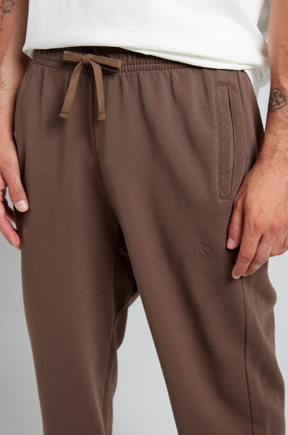 Persona che indossa Essential Sweatpants in Shaved Chocolate con coulisse in vita e tasche laterali, che mette in risalto una vestibilità rilassata | TP_IMAGE_TYPE=MODEL_FRONT