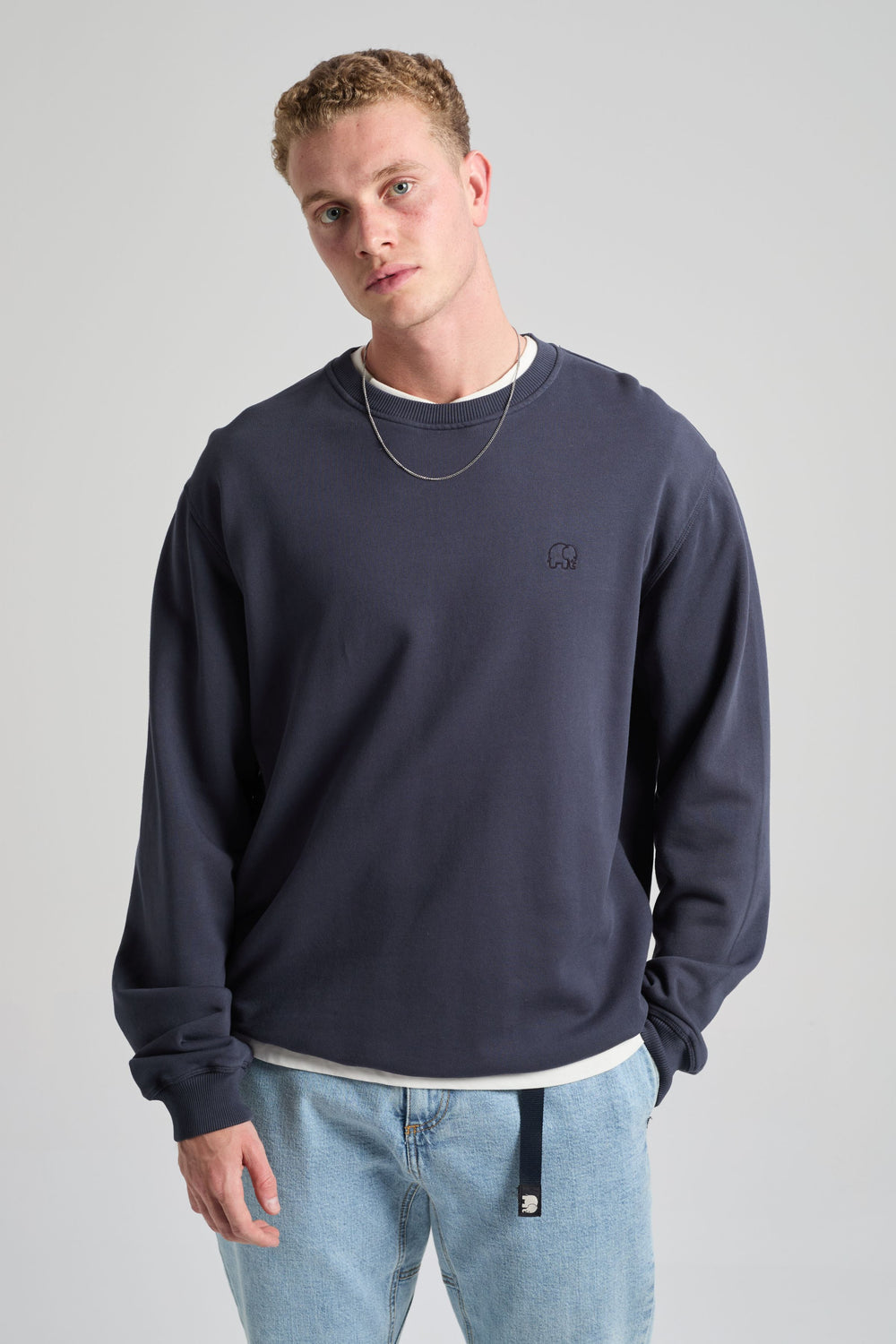 Persona che indossa Essential Sweatshirt in Parisian Blue, a maniche lunghe e con vestibilità rilassata, abbinato a jeans azzurri e una camicia sovrapposta sotto | TP_IMAGE_TYPE=MODEL_FRONT