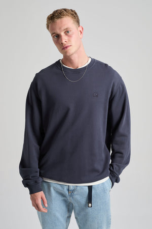 Persona che indossa Essential Sweatshirt in Parisian Blue, a maniche lunghe e con vestibilità rilassata, abbinato a jeans azzurri e una camicia sovrapposta sotto | TP_IMAGE_TYPE=MODEL_FRONT