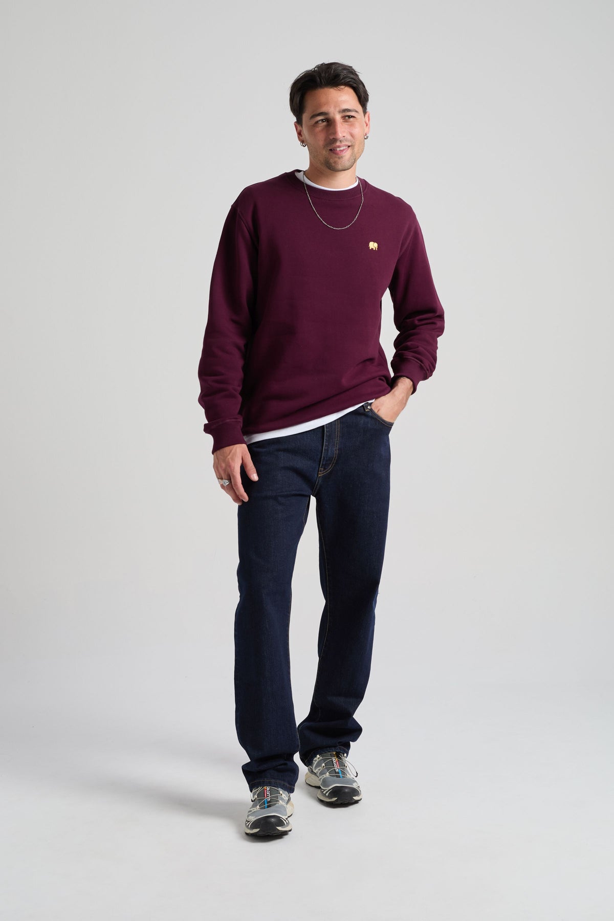 Persona che indossa una Organic Essential Sweatshirt in Wine Red, abbinata a jeans scuri e calzature casual, sorride alla fotocamera | TP_IMAGE_TYPE=MODEL_FRONT