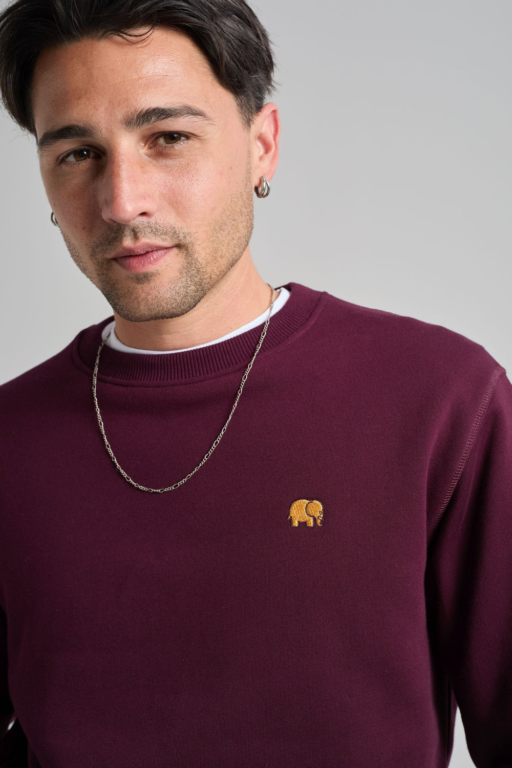 Persona che indossa una felpa Essentials biologica rosso vino, con un piccolo logo elefante ricamato, abbinata a una collana a catena in argento. | TP_IMAGE_TYPE=MODEL_FRONT