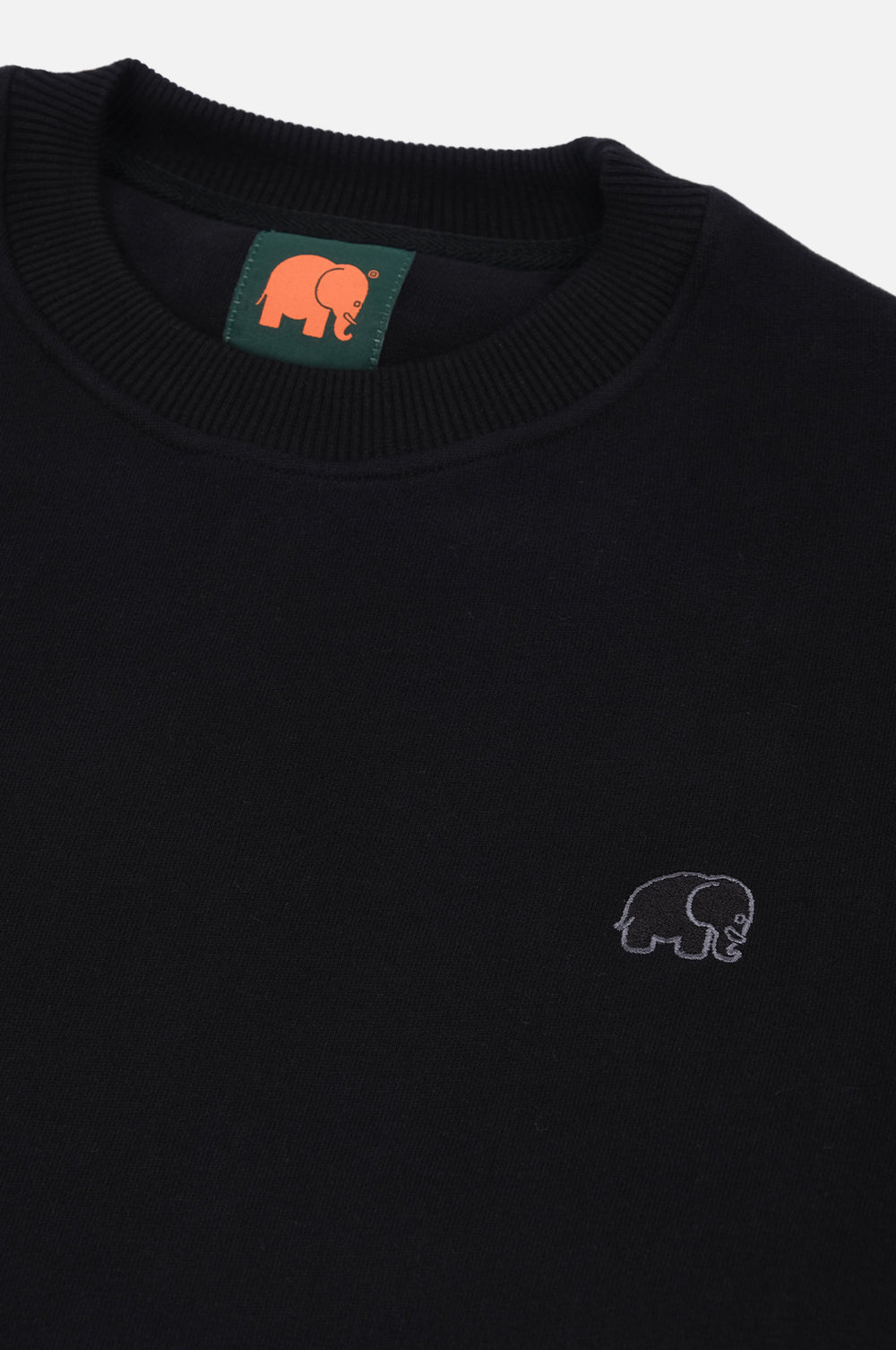 Dettaglio in primo piano della Organic Essential Sweatshirt in nero, con un piccolo logo elefante ricamato e scollo a costine. | TP_IMAGE_TYPE=DETAIL