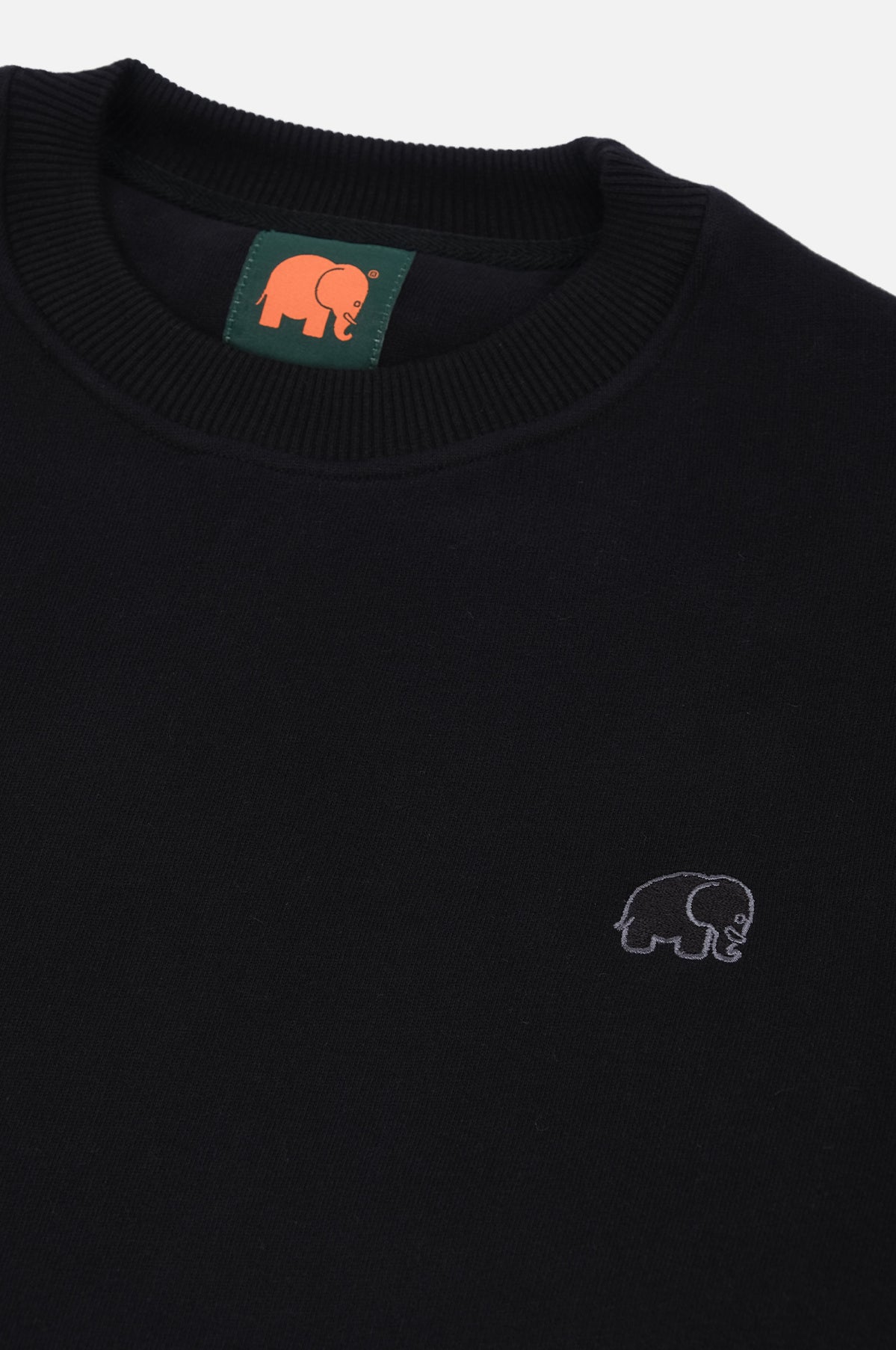 Dettaglio in primo piano della Organic Essential Sweatshirt in nero, con un piccolo logo elefante ricamato e scollo a costine. | TP_IMAGE_TYPE=DETAIL