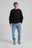 Persona che indossa una Organic Essential Sweatshirt nera, abbinata a jeans azzurri e sneakers, in piedi davanti a uno sfondo neutro. | TP_IMAGE_TYPE=MODEL_FRONT