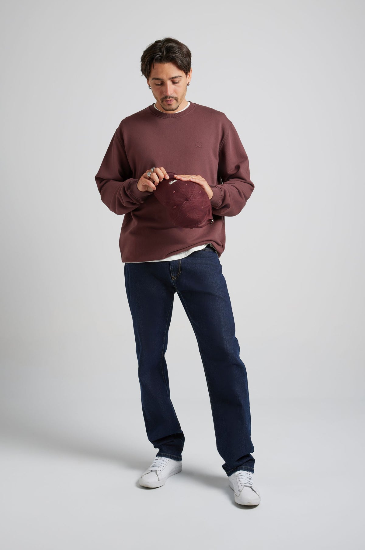 Personne portant l'Essential Sweatshirt en Puce Purple, associé à un jean décontracté et tenant un chapeau | TP_IMAGE_TYPE=MODEL_FRONT