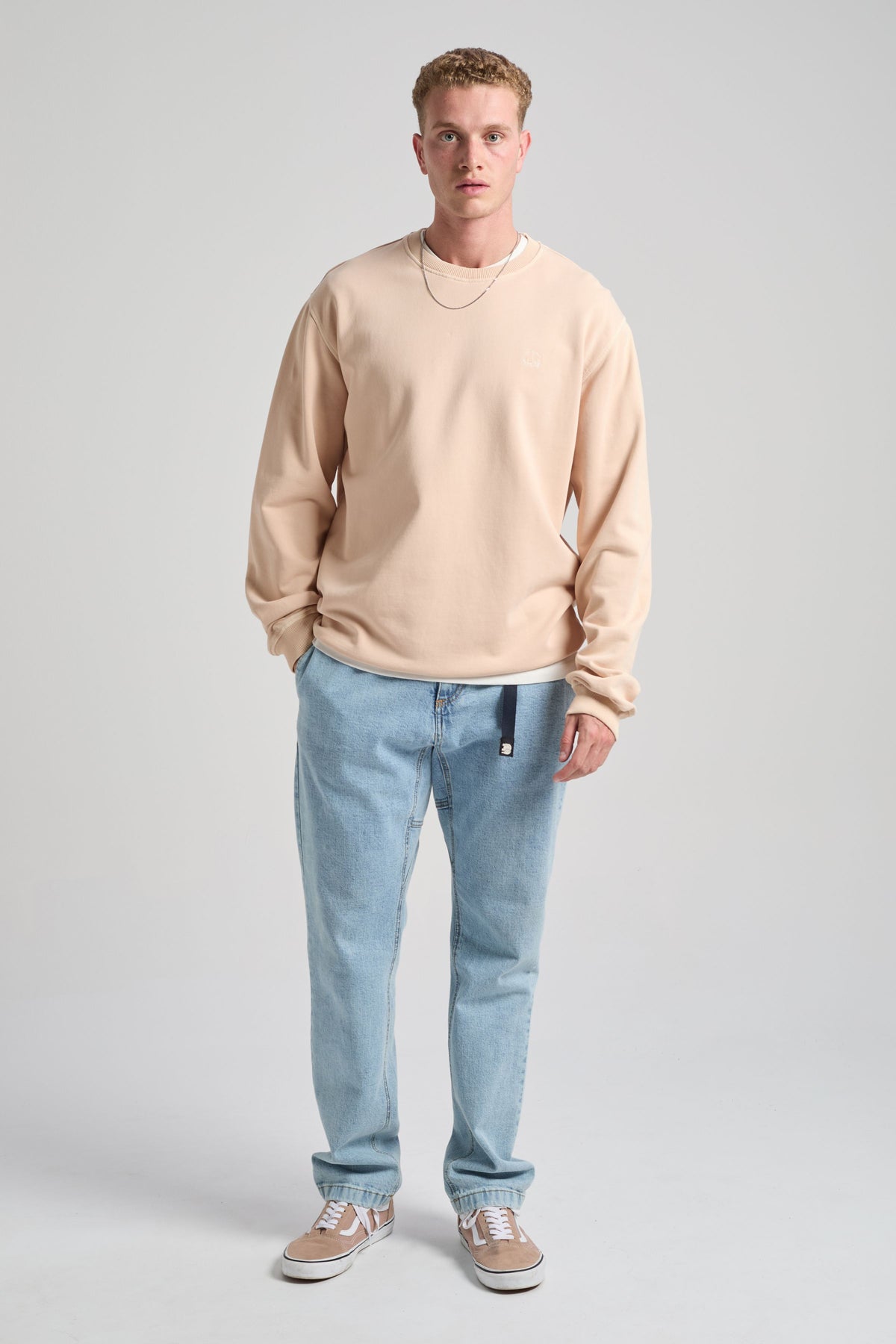 Persona che indossa una Essential Sunwashed Sweatshirt in Smoke Gray, abbinata a jeans azzurri e sneakers casual, in piedi su uno sfondo neutro. | TP_IMAGE_TYPE=MODEL_FRONT