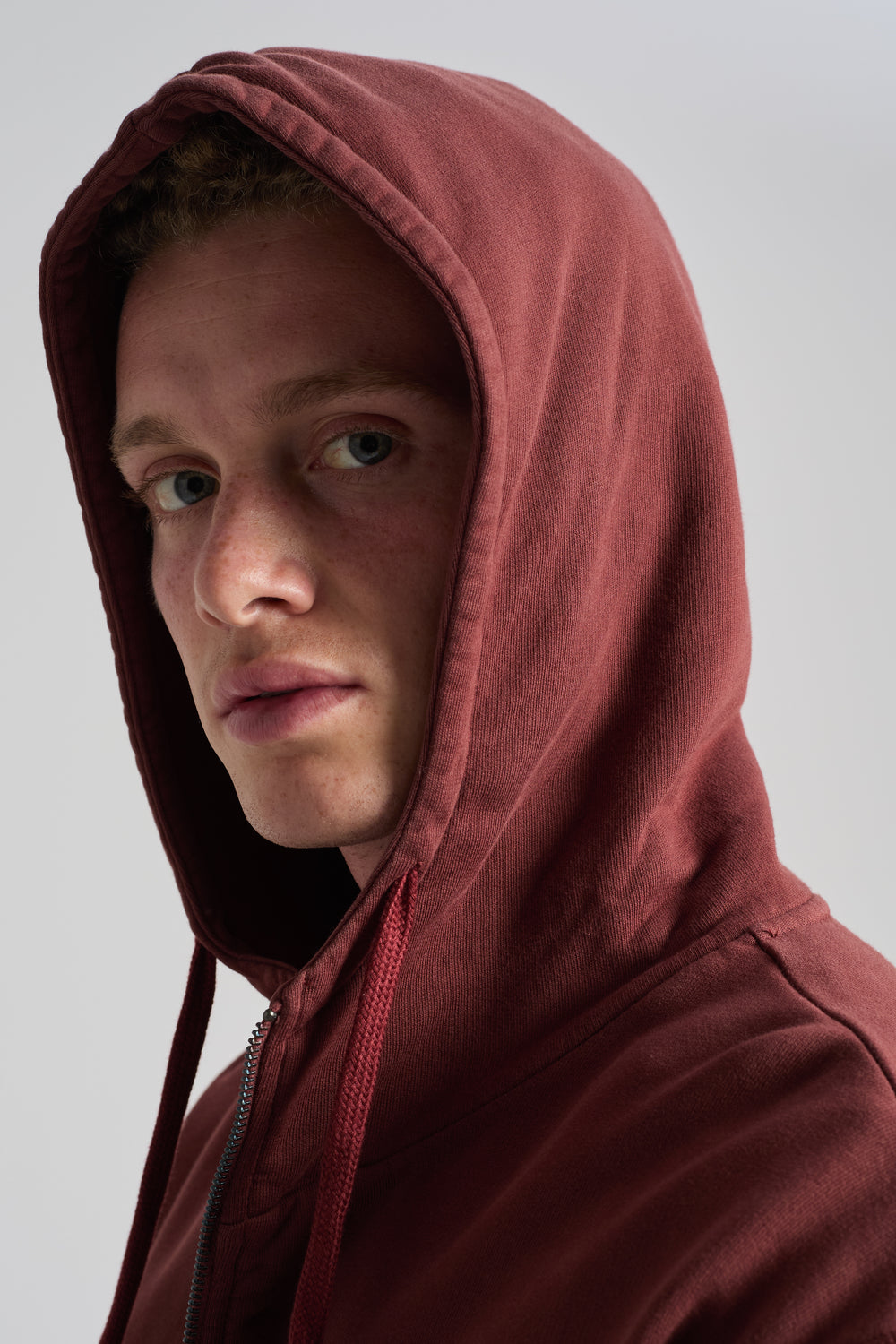 Persona con Essential Zip Hoodie en Andorra Brown y capucha visible, mostrando el detalle de la cremallera | TP_IMAGE_TYPE=MODEL_FRONT