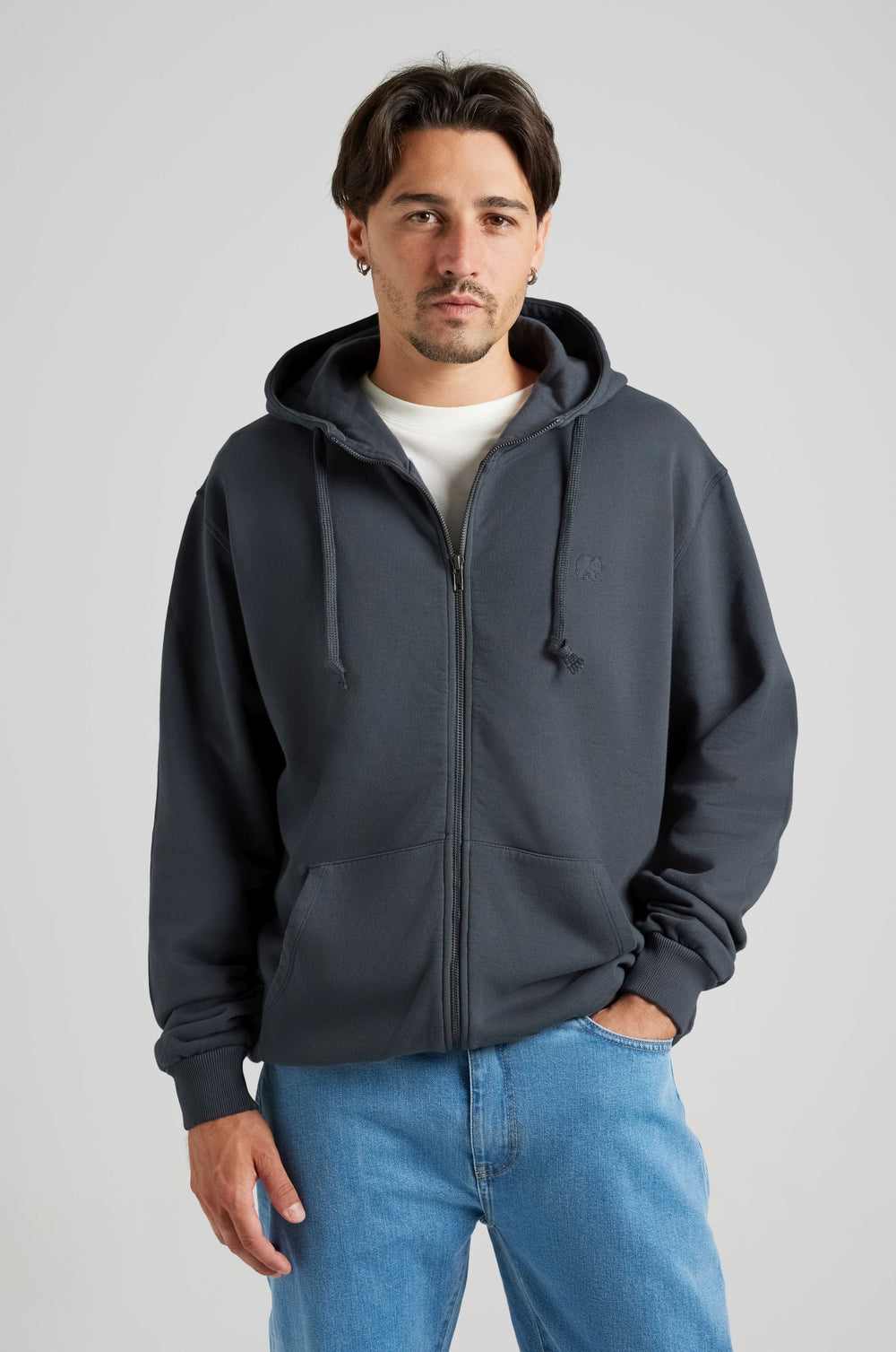 Personne portant un Essential Zip Hoodie en Bitumen Grey, avec fermeture à glissière frontale et capuche, associé à un jean bleu clair. | TP_IMAGE_TYPE=MODEL_FRONT