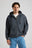 Personne portant un Essential Zip Hoodie en Bitumen Grey, avec fermeture à glissière frontale et capuche, associé à un jean bleu clair. | TP_IMAGE_TYPE=MODEL_FRONT