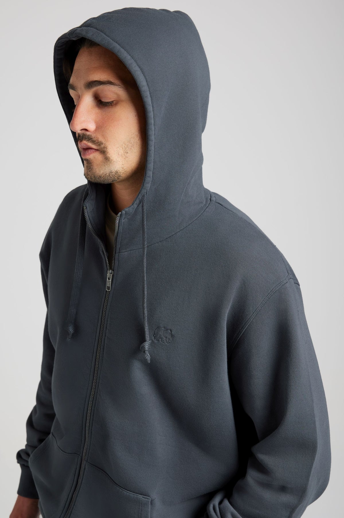 Personne portant un Essential Zip Hoodie en Bitumen Grey, avec capuche et fermeture à glissière frontale, vue en gros plan. | TP_IMAGE_TYPE=MODEL_FRONT