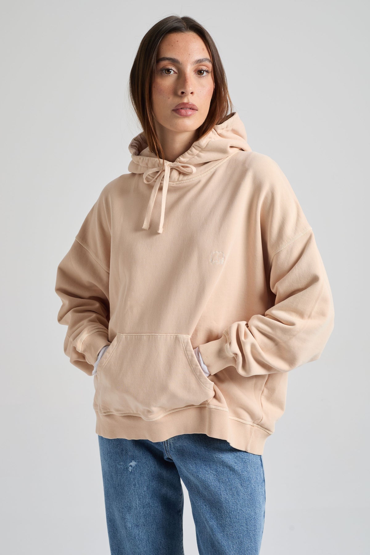 Personne portant un sweat à capuche beige et un jean bleu sur fond uni. TP_IMAGE_TYPE=MODEL_FRONT