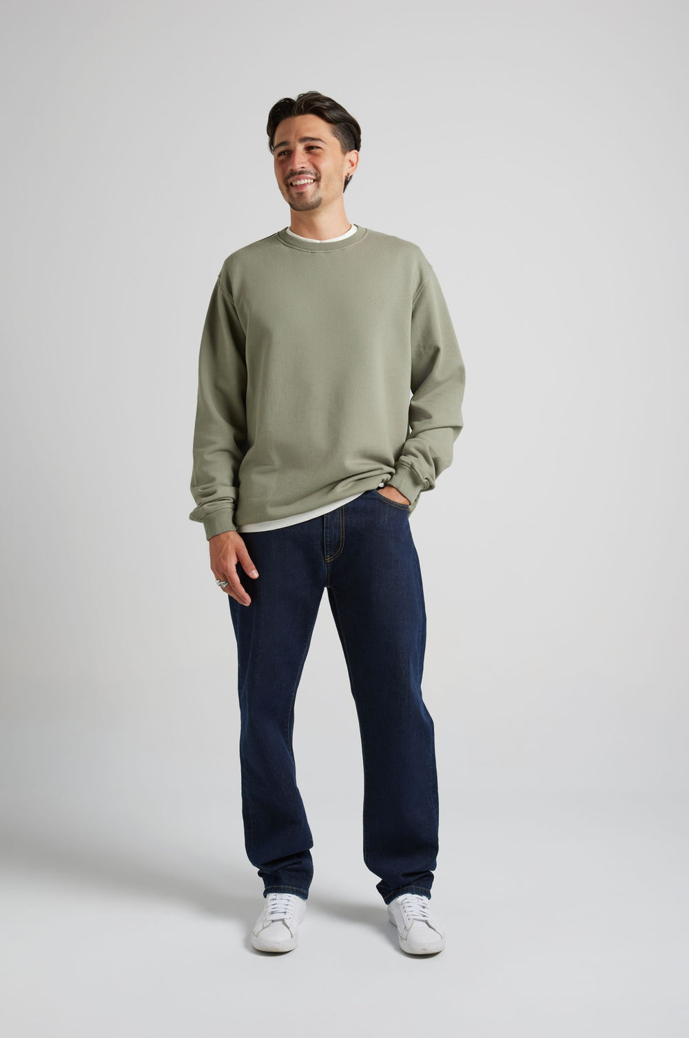 Personne portant un sweat-shirt essentiel en Agave Green, associé à un jean en denim foncé et des baskets blanches, souriant dans une pose de vue de face. | TP_IMAGE_TYPE=MODEL_FRONT