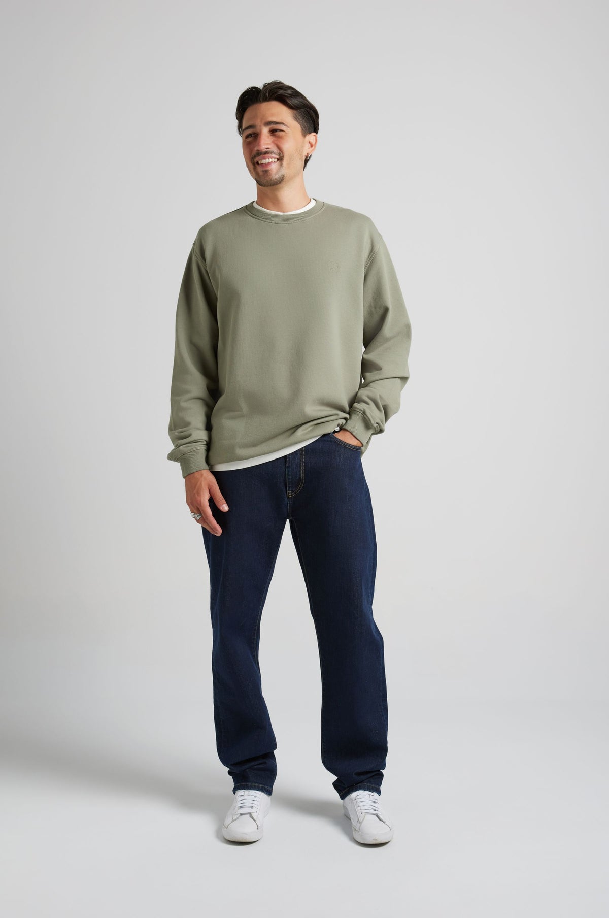 Personne portant un sweat-shirt essentiel en Agave Green, associé à un jean en denim foncé et des baskets blanches, souriant dans une pose de vue de face. | TP_IMAGE_TYPE=MODEL_FRONT