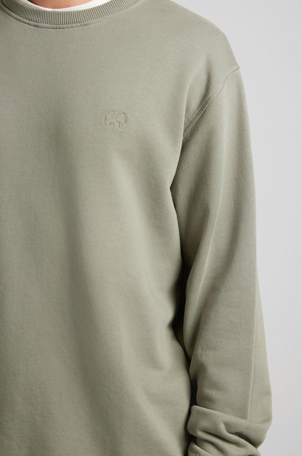 Personne portant l'Essential Sweatshirt en Agave Green, arborant un discret logo éléphant sur la poitrine | TP_IMAGE_TYPE=MODEL_FRONT