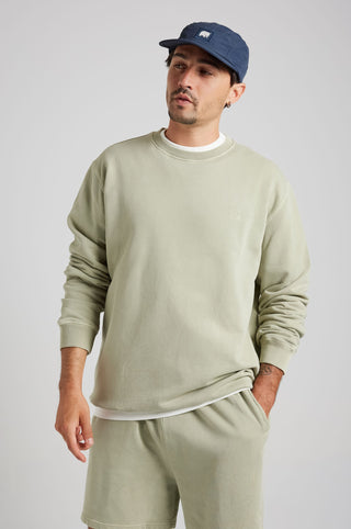 Personne portant un Essential Sunwashed Sweatshirt en coloris Seagrass, associé à un short confortable et une casquette, dans une pose décontractée sur un fond neutre. | TP_IMAGE_TYPE=MODEL_FRONT