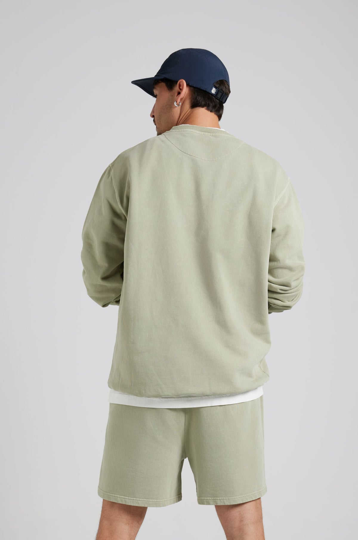 Personne portant un Essential Sunwashed Sweatshirt en Seagrass, vue de dos, assorti à un short coordonné et une casquette. | TP_IMAGE_TYPE=MODEL_BACK
