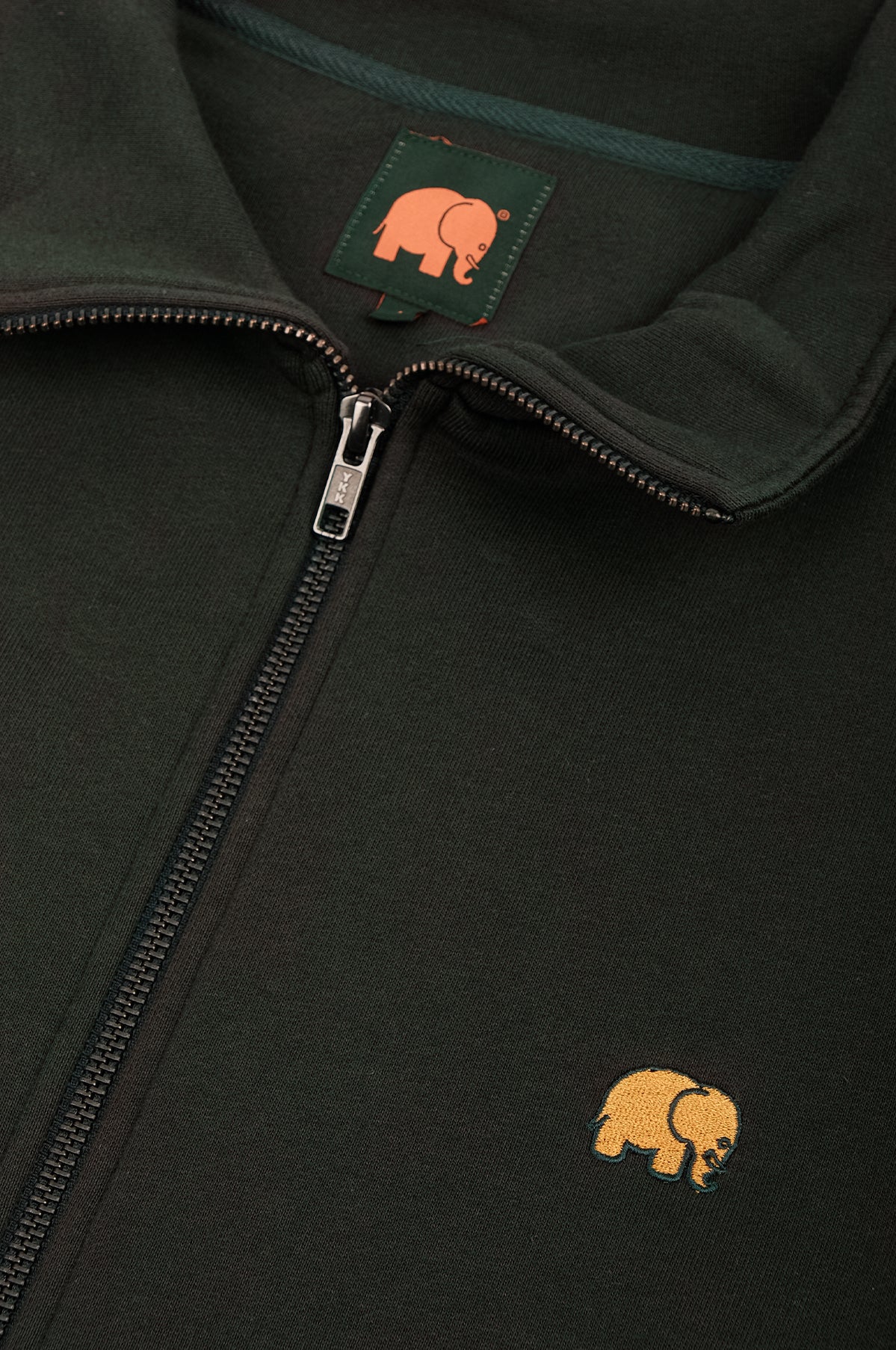 Détail en gros plan de l'Organic Essential Zip Sweatshirt en Scarab Green, montrant la fermeture éclair et le logo éléphant brodé. | TP_IMAGE_TYPE=DETAIL