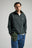 Personne portant un Organic Essential Zip Sweatshirt en Scarab Green, associé à une casquette verte assortie et à un jean bleu, debout devant un fond neutre. | TP_IMAGE_TYPE=MODEL_FRONT
