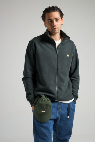 Personne portant un Organic Essential Zip Sweatshirt en Scarab Green, associé à une casquette verte assortie et à un jean bleu, debout devant un fond neutre. | TP_IMAGE_TYPE=MODEL_FRONT