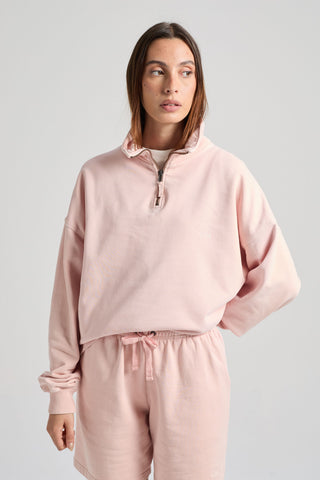 Persona che indossa una Sunwashed Essential Quarter Zip Sweatshirt da donna in lotus pink, abbinata a shorts coordinati, con lo sguardo rivolto di lato su sfondo neutro. | TP_IMAGE_TYPE=MODEL_FRONT