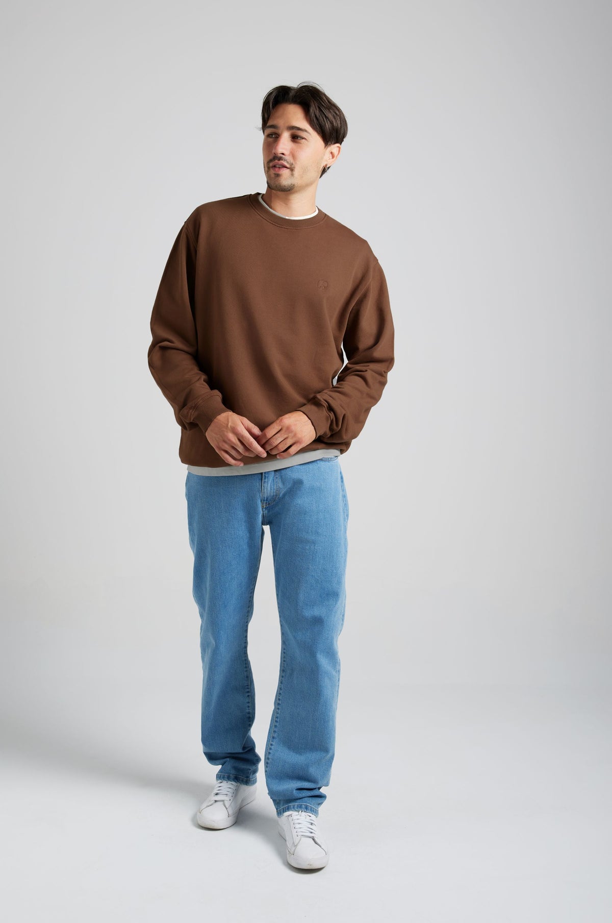 Person wearing Essential Sweatshirt in Carafe Brown, paired with light blue jeans and white sneakers, standing in a neutral background | TP_IMAGE_TYPE=MODEL_FRONT