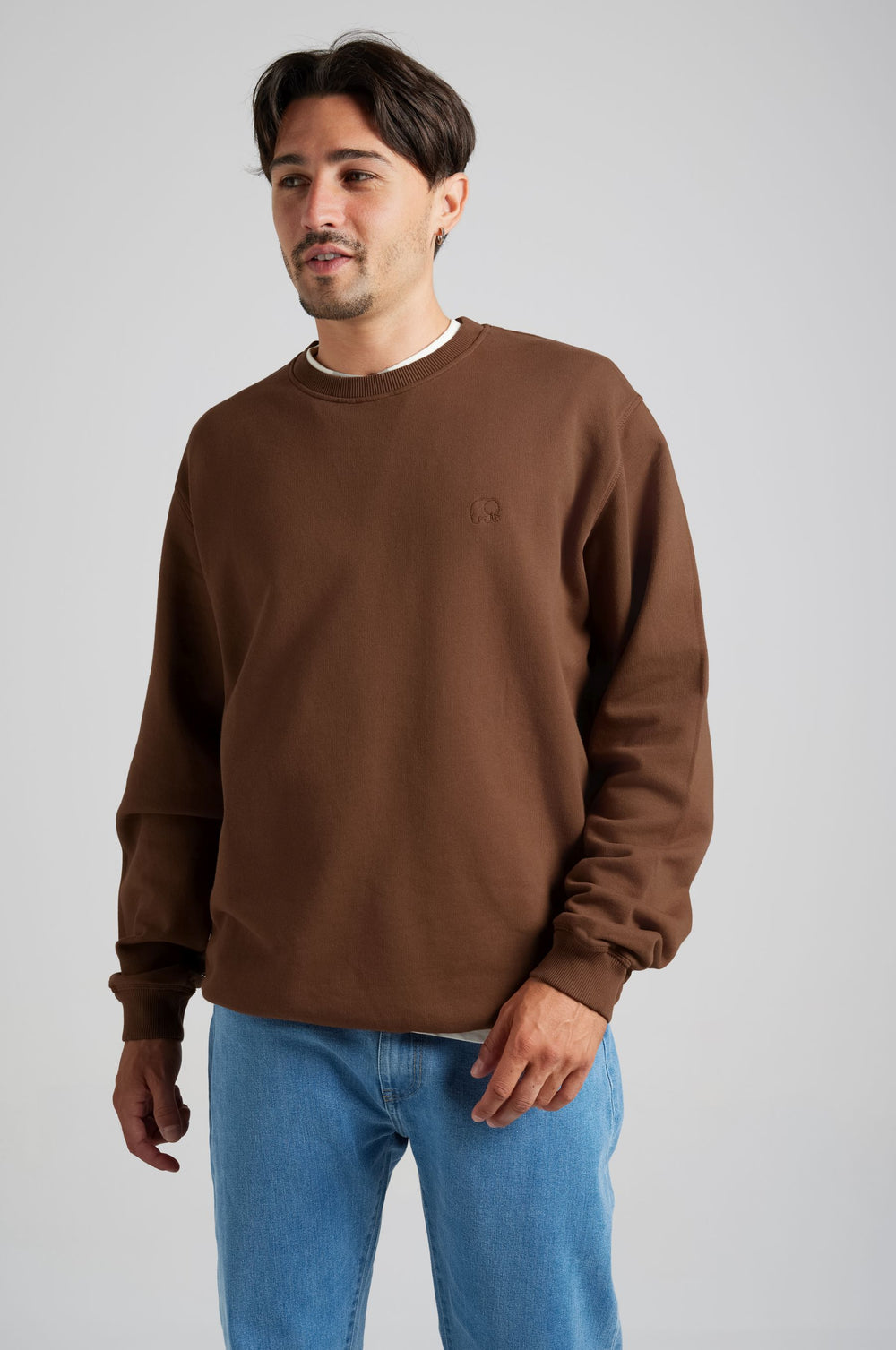Person wearing an Essential Sweatshirt in Carafe Brown, paired with light blue jeans, standing against a neutral background. | TP_IMAGE_TYPE=MODEL_FRONT