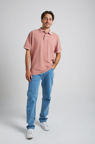 Persona che indossa la polo Essential Sunwashed Polo nel colore Old Rose con jeans azzurri e sneakers bianche, in piedi di fronte su uno sfondo neutro | TP_IMAGE_TYPE=MODEL_FRONT