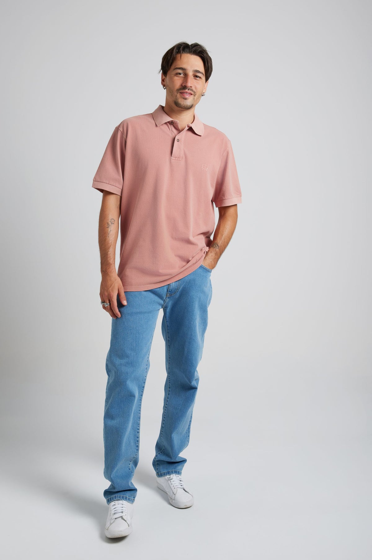 Persona che indossa la polo Essential Sunwashed Polo nel colore Old Rose con jeans azzurri e sneakers bianche, in piedi di fronte su uno sfondo neutro | TP_IMAGE_TYPE=MODEL_FRONT