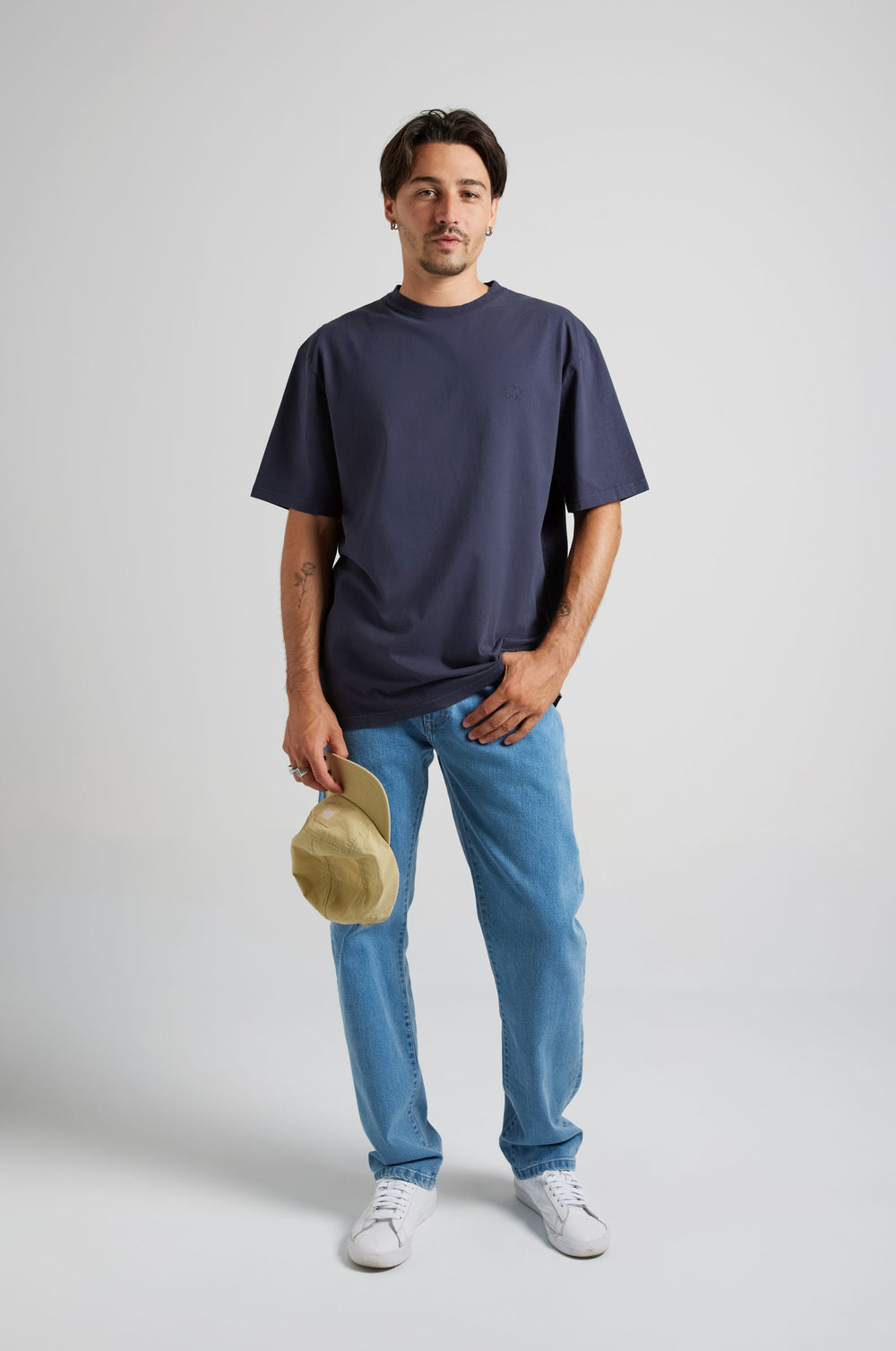 Personne portant un Essential T-Shirt en Parisian Blue, associé à un jean bleu clair et tenant une casquette à la main. | TP_IMAGE_TYPE=MODEL_FRONT