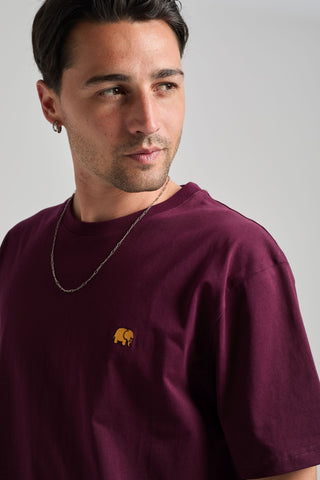 Persona che indossa una Organic Essential T-Shirt in Wine Red, con una vista ravvicinata del design | TP_IMAGE_TYPE=MODEL_FRONT