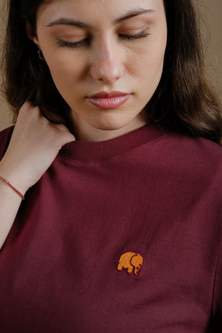 Persona che indossa una Women's Organic Essential T-Shirt bordeaux, con vista dettagliata del logo elefante ricamato | TP_IMAGE_TYPE=MODEL_FRONT