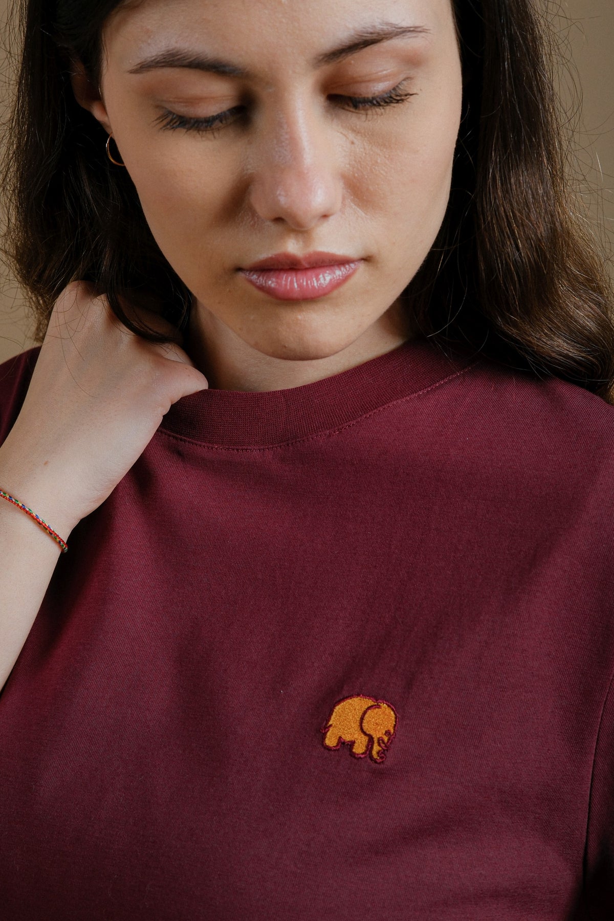 Persona che indossa una Women's Organic Essential T-Shirt bordeaux, con vista dettagliata del logo elefante ricamato | TP_IMAGE_TYPE=MODEL_FRONT