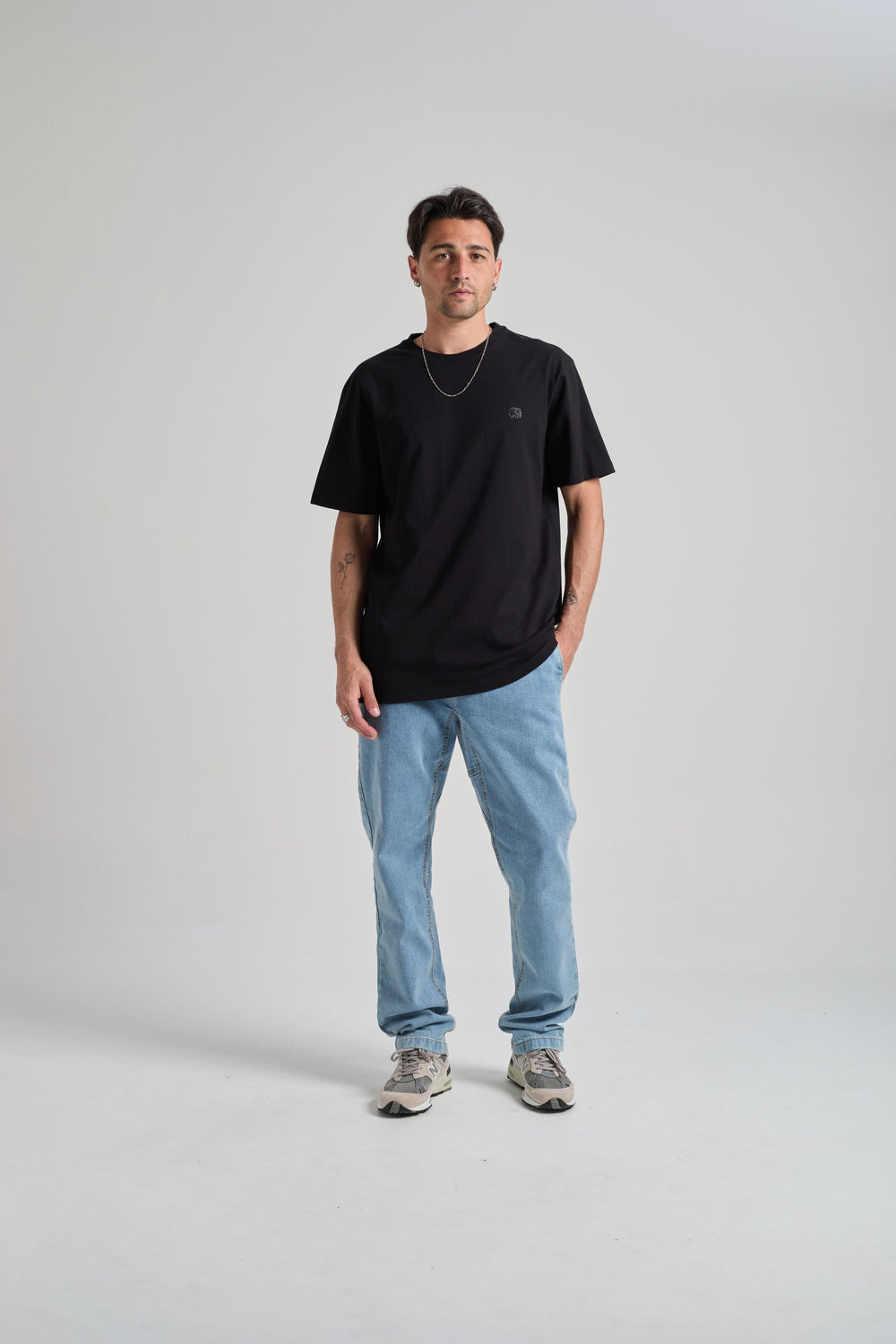 Personne portant un t-shirt essential biologique en noir, associé à un jean bleu clair et des baskets, debout devant un fond neutre. | TP_IMAGE_TYPE=MODEL_FRONT