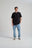 Personne portant un t-shirt essential biologique en noir, associé à un jean bleu clair et des baskets, debout devant un fond neutre. | TP_IMAGE_TYPE=MODEL_FRONT