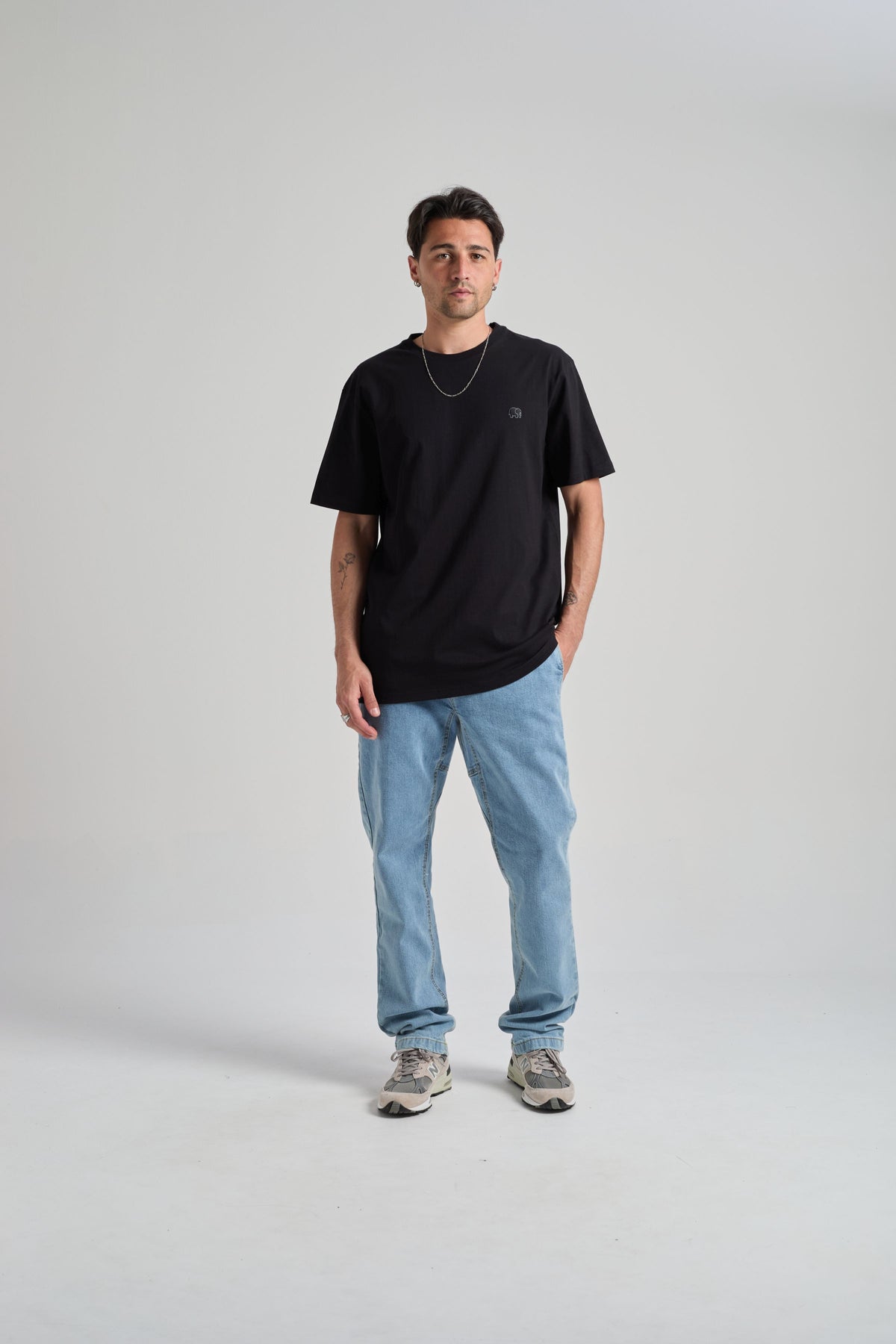 Personne portant un t-shirt essential biologique en noir, associé à un jean bleu clair et des baskets, debout devant un fond neutre. | TP_IMAGE_TYPE=MODEL_FRONT