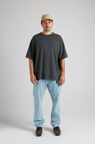 Personne portant un t-shirt oversize en tissu épais coloris Pirate Black, associé à un jean bleu clair et une casquette, debout devant un fond neutre. | TP_IMAGE_TYPE=MODEL_FRONT
