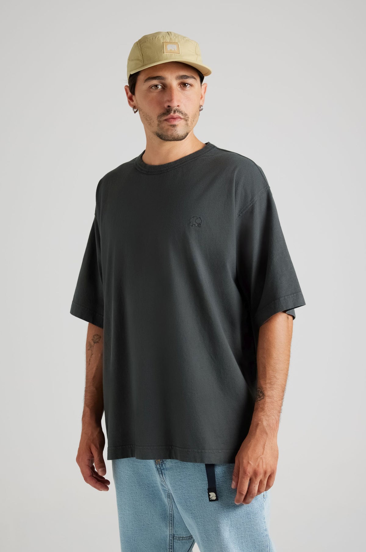 Person in einem übergroßen Heavyweight-T-Shirt in Pirate Black, kombiniert mit einer hellblauen Jeans und einer beigen Cap, vor neutralem Hintergrund stehend. | TP_IMAGE_TYPE=MODEL_FRONT