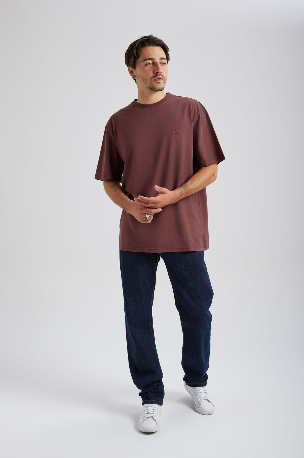 Person wearing an Essential T-Shirt in Puce Purple, styled with dark denim pants and white sneakers, standing casually with hands positioned in front. | TP_IMAGE_TYPE=MODEL_FRONT