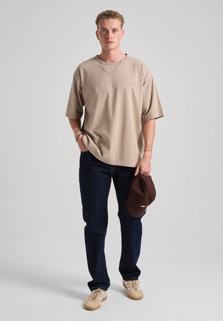 Personne portant un Essential Oversized T-Shirt en Moon Rock Grey, avec un jean foncé et tenant une casquette marron | TP_IMAGE_TYPE=MODEL_FRONT