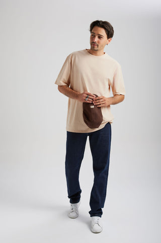 Personne portant un Essential Sunwashed T-Shirt en Smoke Gray, associé à un jean bleu et tenant une casquette marron. | TP_IMAGE_TYPE=MODEL_FRONT