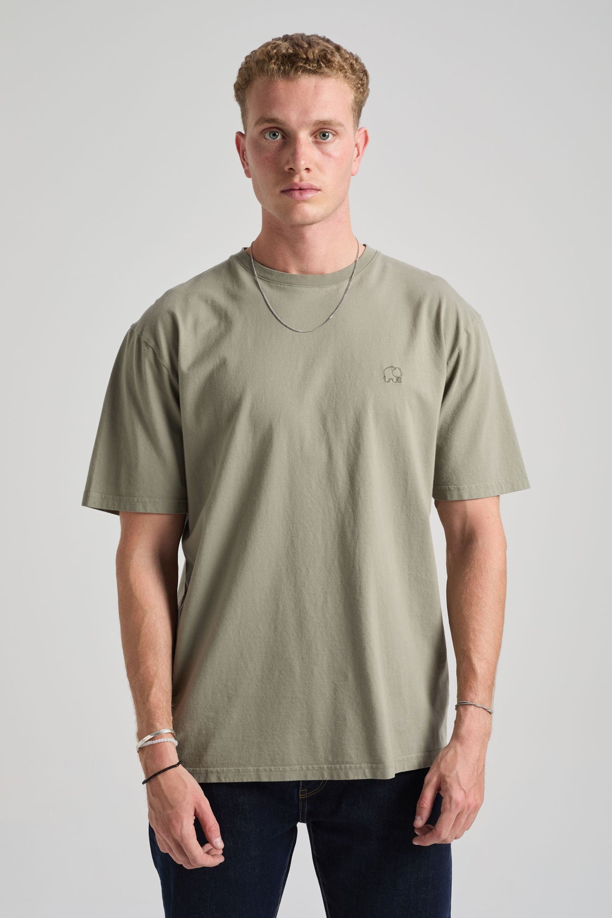 Person wearing an essential t-shirt in Agave Green, featuring a relaxed fit and short sleeves, styled with dark jeans and a necklace. | TP_IMAGE_TYPE=MODEL_FRONT