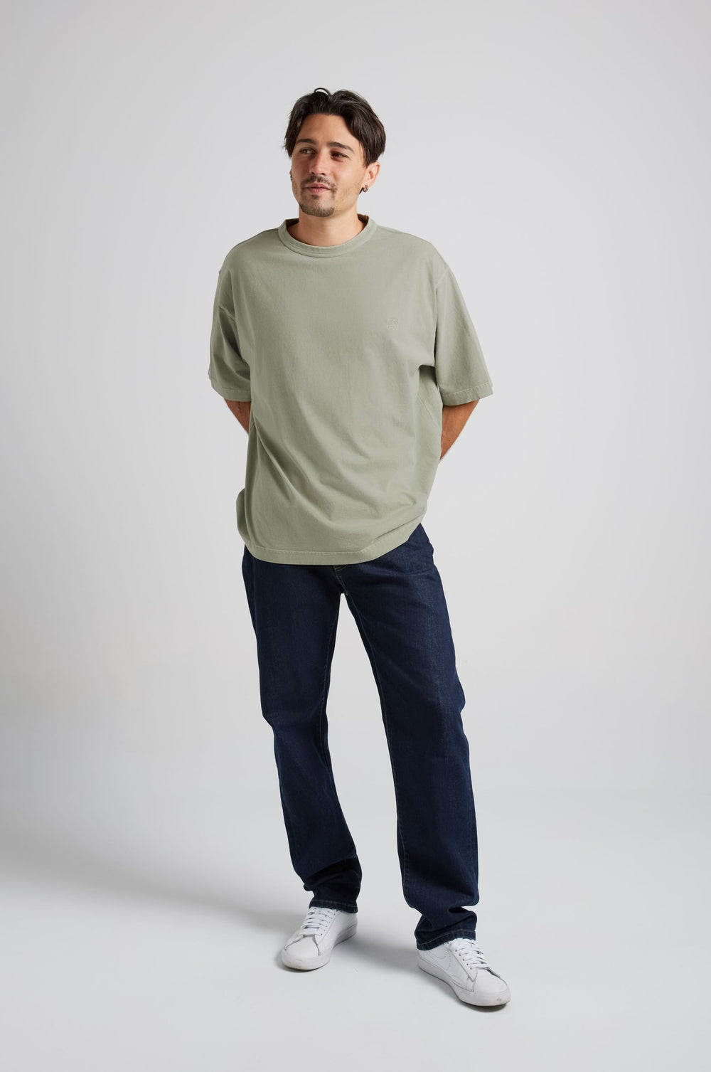 Persona che indossa una Essential Sunwashed Heavyweight Oversized T-Shirt in Seagrass, abbinata a jeans scuri e sneakers bianche, in piedi con le mani dietro la schiena. | TP_IMAGE_TYPE=MODEL_FRONT