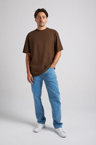 Person wearing an Essential T-Shirt in Carafe Brown paired with light blue jeans and white sneakers, standing in a relaxed pose. | TP_IMAGE_TYPE=MODEL_FRONT