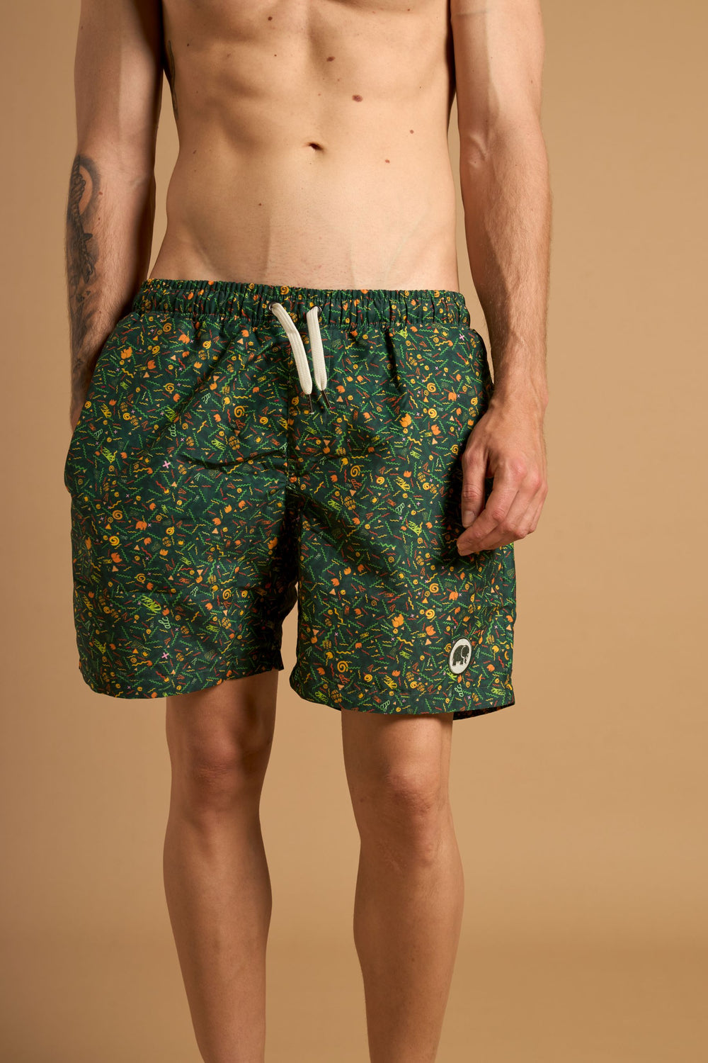 Personne portant le Dogtown SEAQUAL®YARN Swim Trunks dans un motif vert éclatant aux multiples dessins colorés, en pose sur un fond neutre | TP_IMAGE_TYPE=MODEL_FRONT
