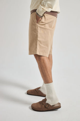 Persona che indossa Ecodye Cotton Climber Shorts Sand, vista laterale con le mani nelle tasche e scarpe completate da calzini bianchi | TP_IMAGE_TYPE=MODEL_FRONT