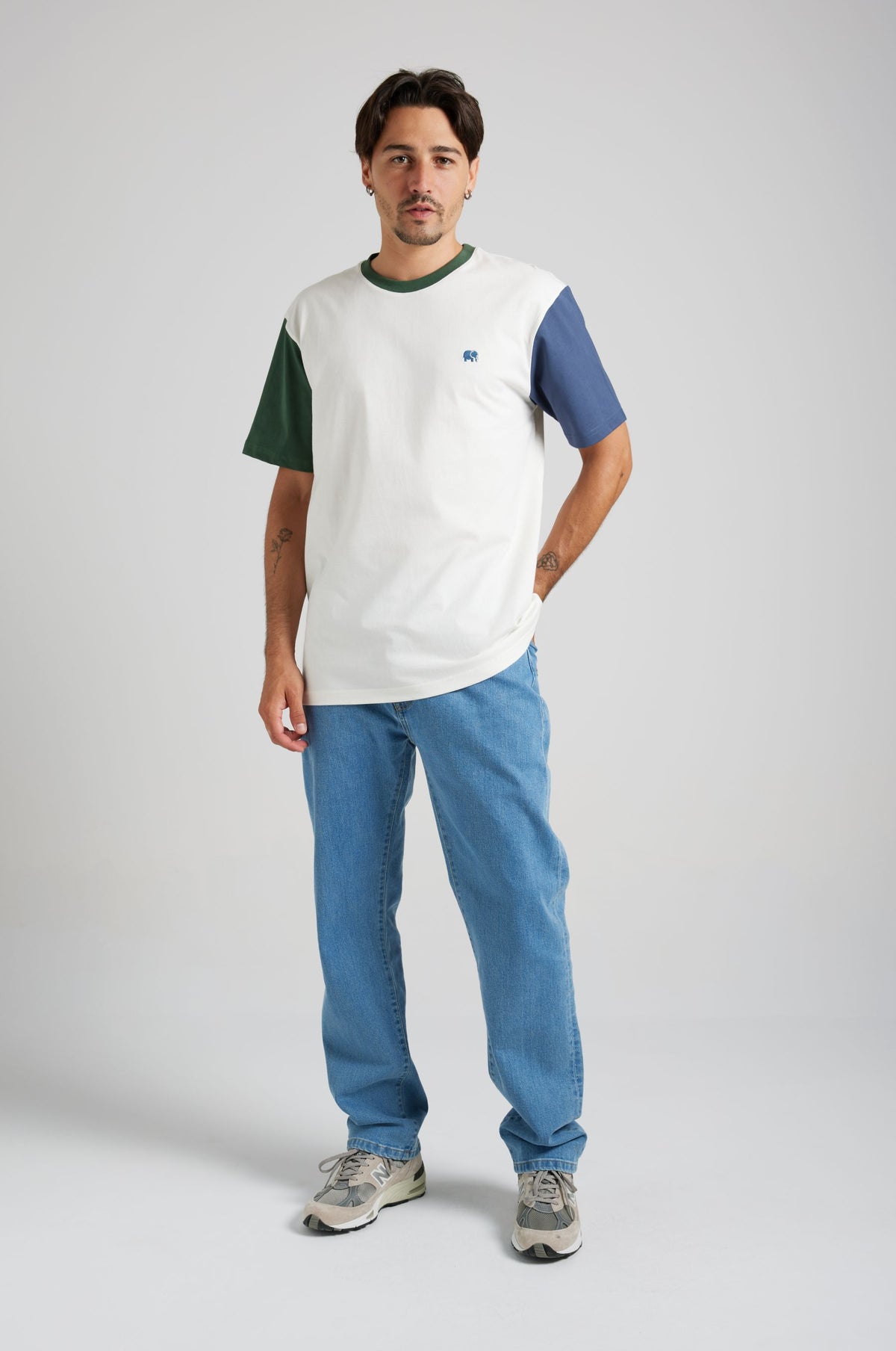 Persona che indossa una t-shirt biologica color block dalle tonalità naturali, con maniche verdi e blu, abbinata a jeans blu. | TP_IMAGE_TYPE=MODEL_FRONT